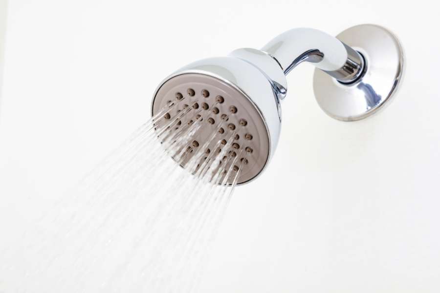 Pommeau de douche fixe chromé avec jets d'eau puissants sur fond blanc, un équipement propre et bien entretenu.