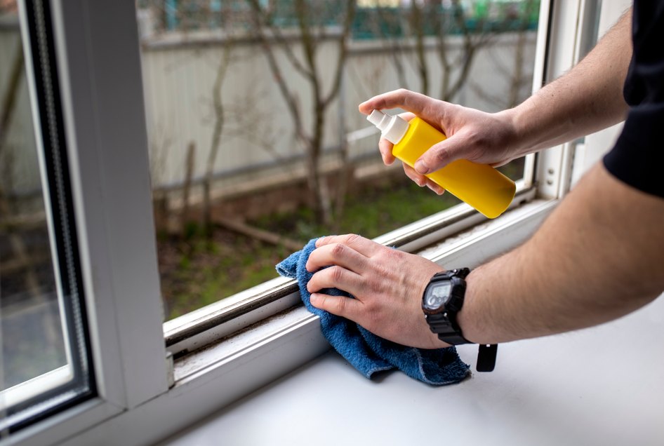 Un homme applique un produit de traitement anti uv jaunissement menuiserie pvc sur le cadre d'une fenêtre.