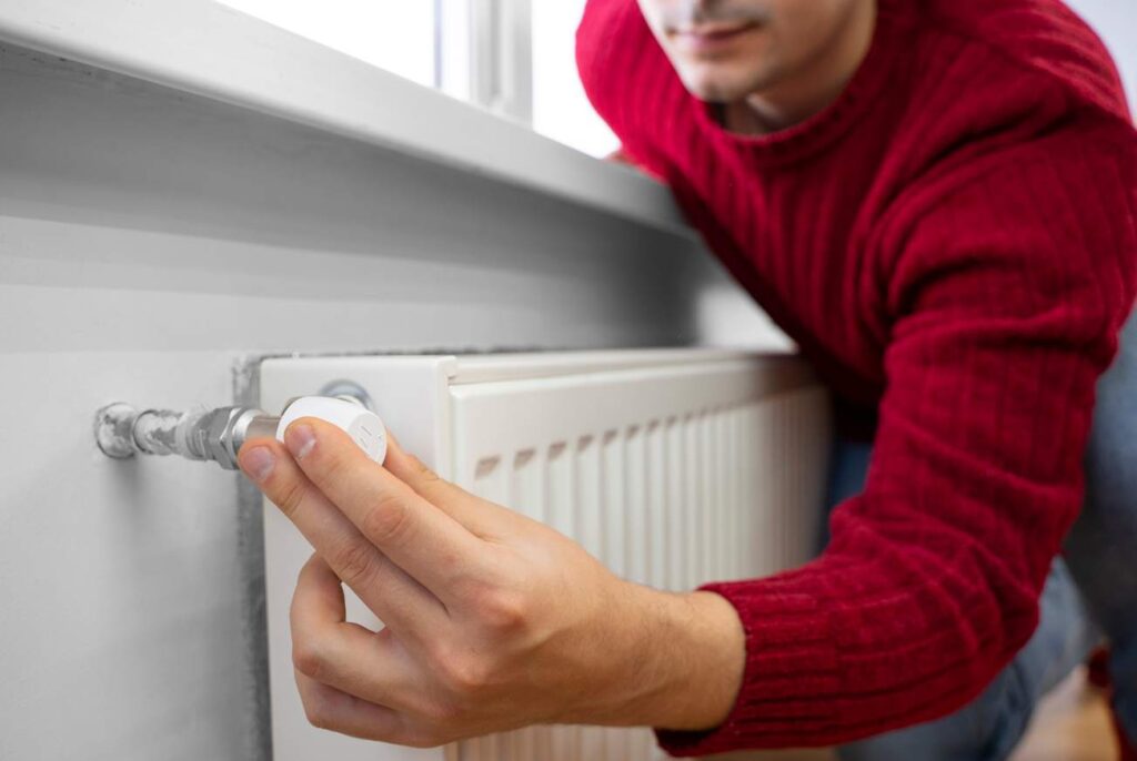 Un homme ajuste la température sur un radiateur blanc pour illustrer la différence chauffage collectif et individuel